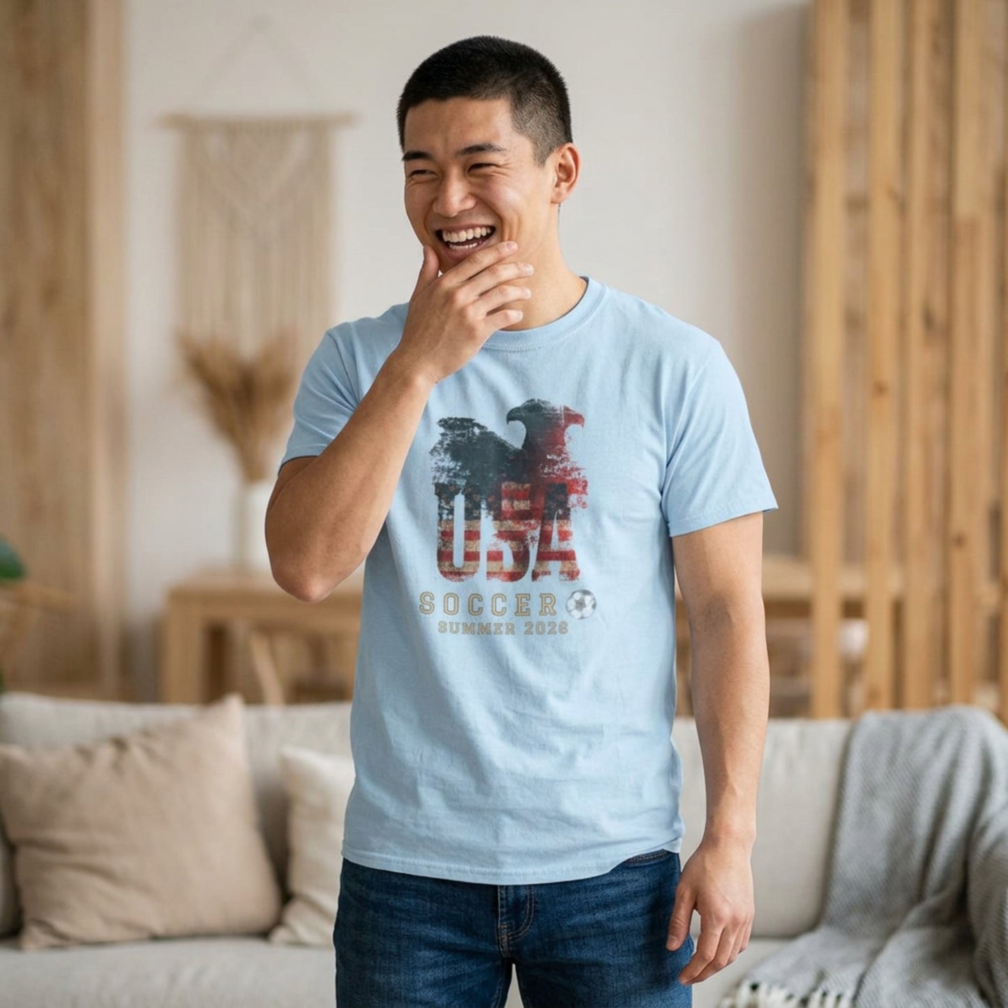 Man wearing a light blue t-shirt with 'USA Soccer Summer 2020' design in a living room.