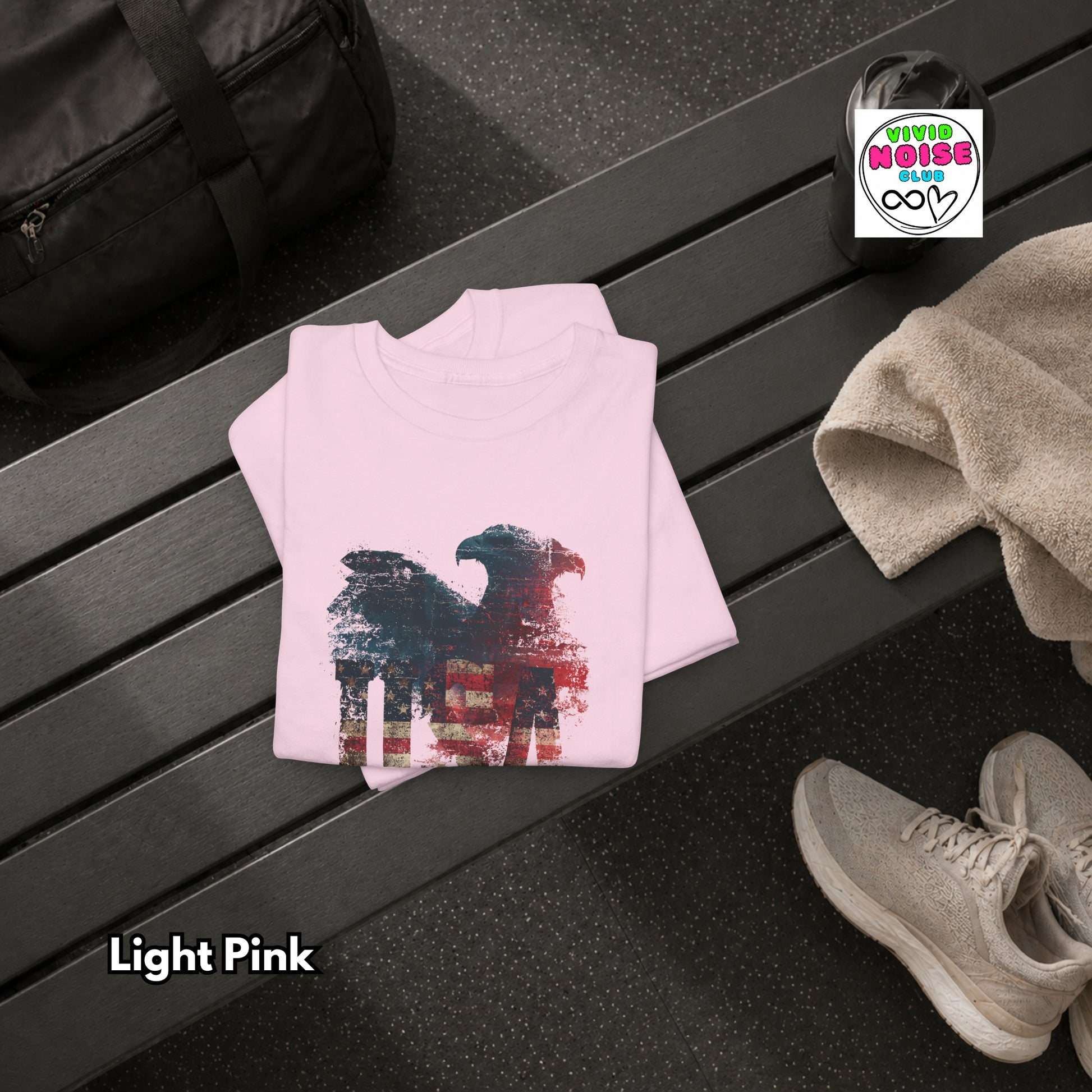 Light pink sweatshirt with a graphic design on a black surface, next to a black bag and beige shoes.