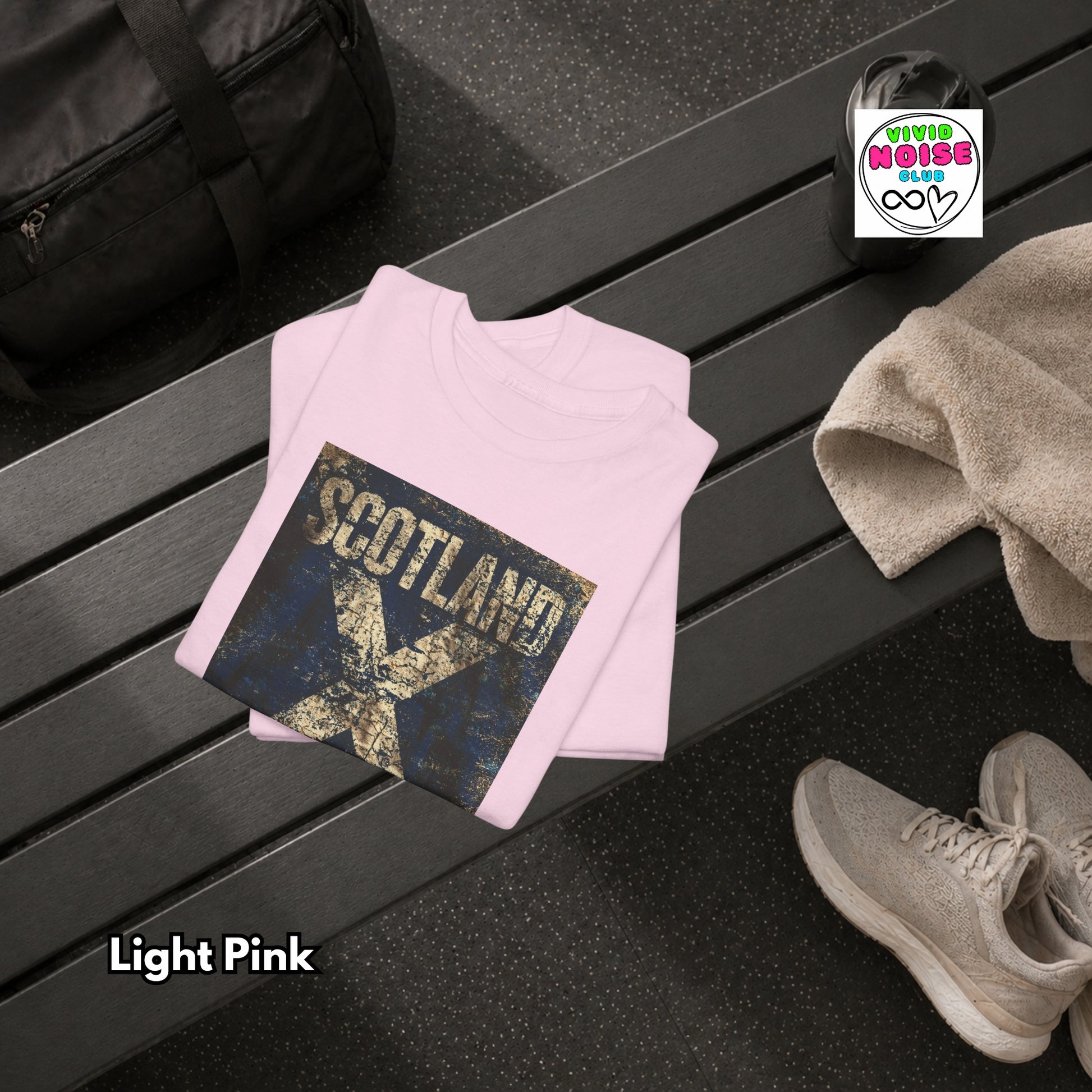 Light pink sweatshirt with 'Scotland' design on a black surface, next to a black bag and beige shoes.