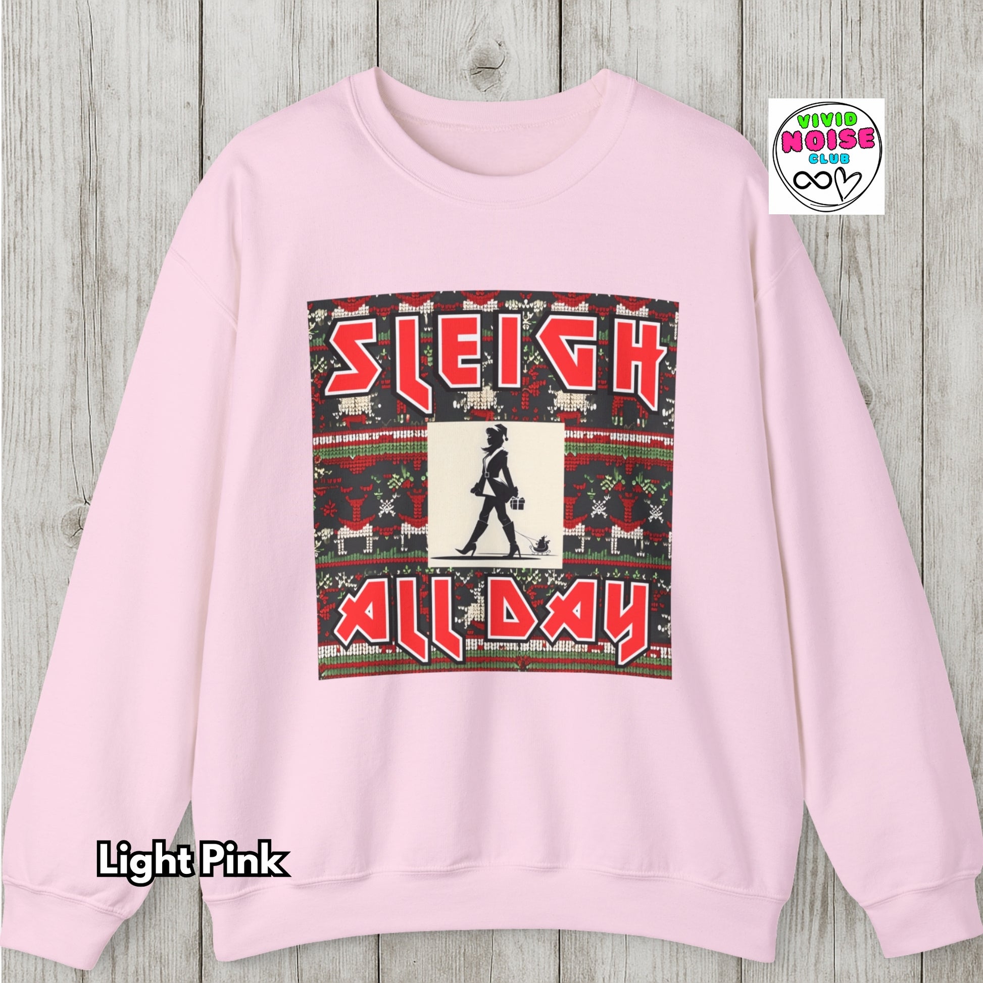 Light pink sweatshirt with Christmas-themed graphic and 'Sleigh All Day' text on a wooden surface.