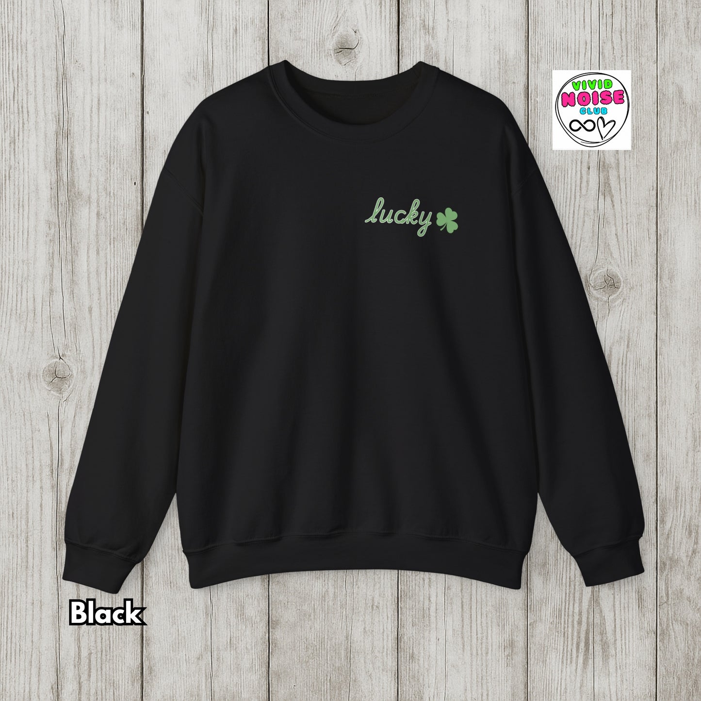 Black sweatshirt with 'lucky' and a clover design on a wooden surface, featuring the Vivid Noise brand.