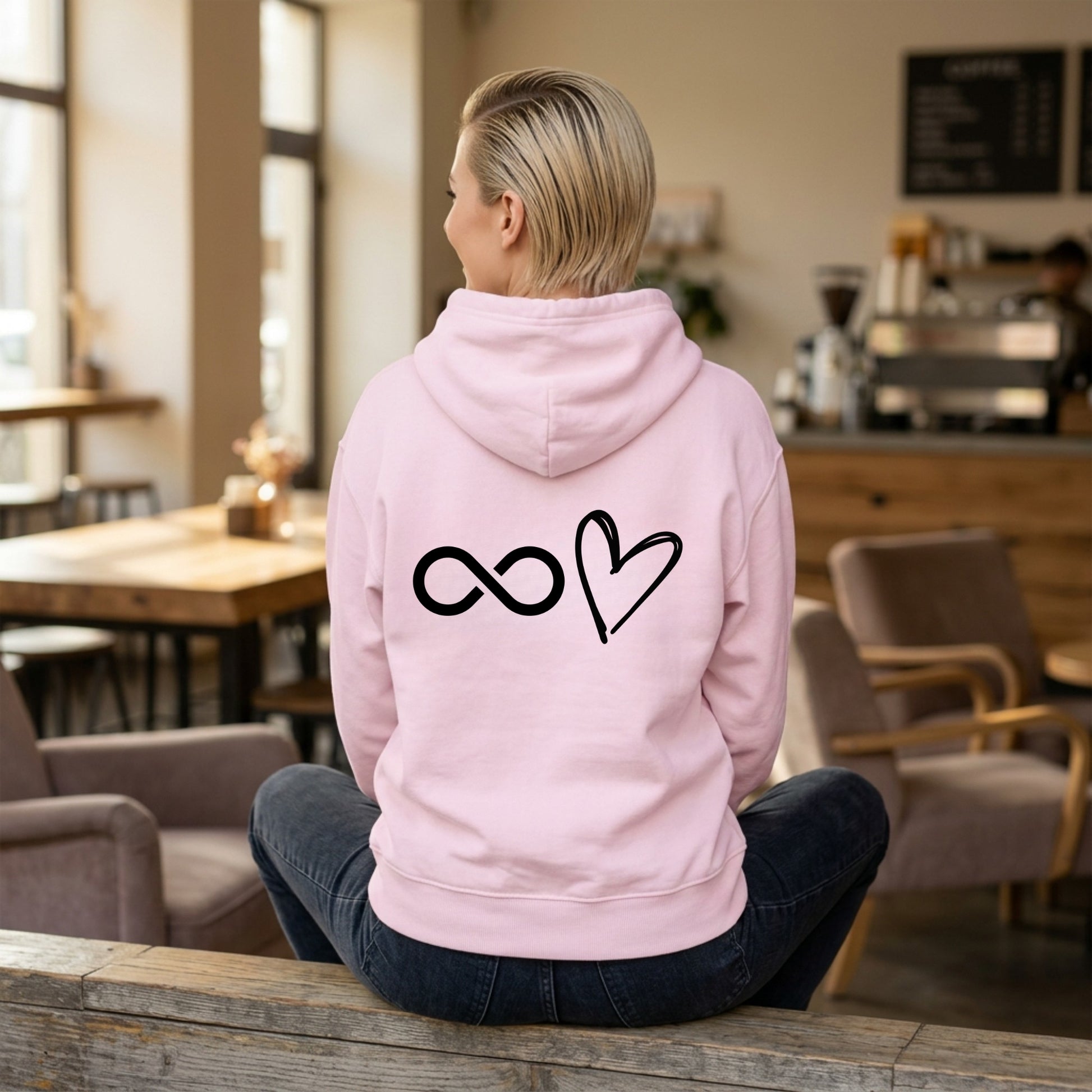 Person wearing a pink hoodie with infinity and heart symbols in a cafe.