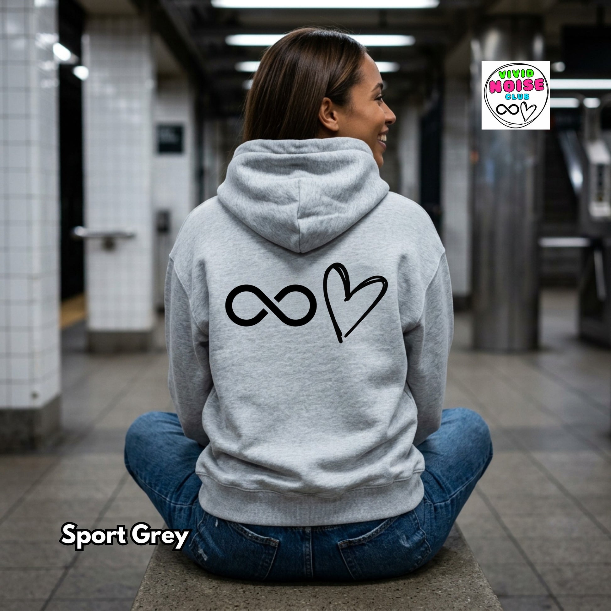 Person wearing a gray hoodie with a symbol on the back, sitting in a subway station.