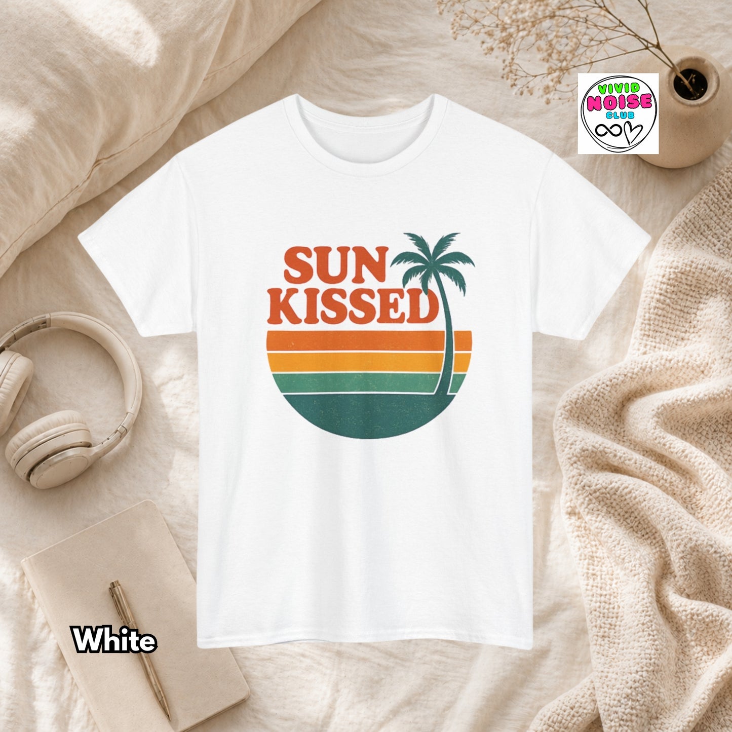 White t-shirt with 'Sun Kissed' design on a textured surface with accessories.