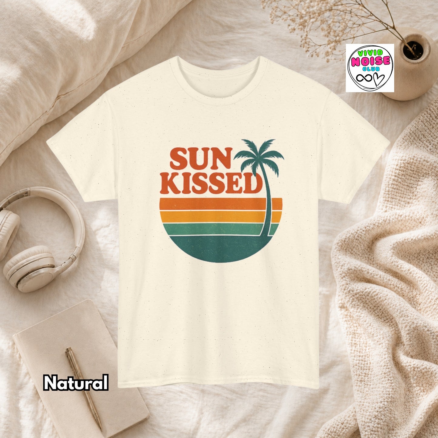 Natural beige t-shirt with 'Sun Kissed' graphic design on a textured surface with accessories.