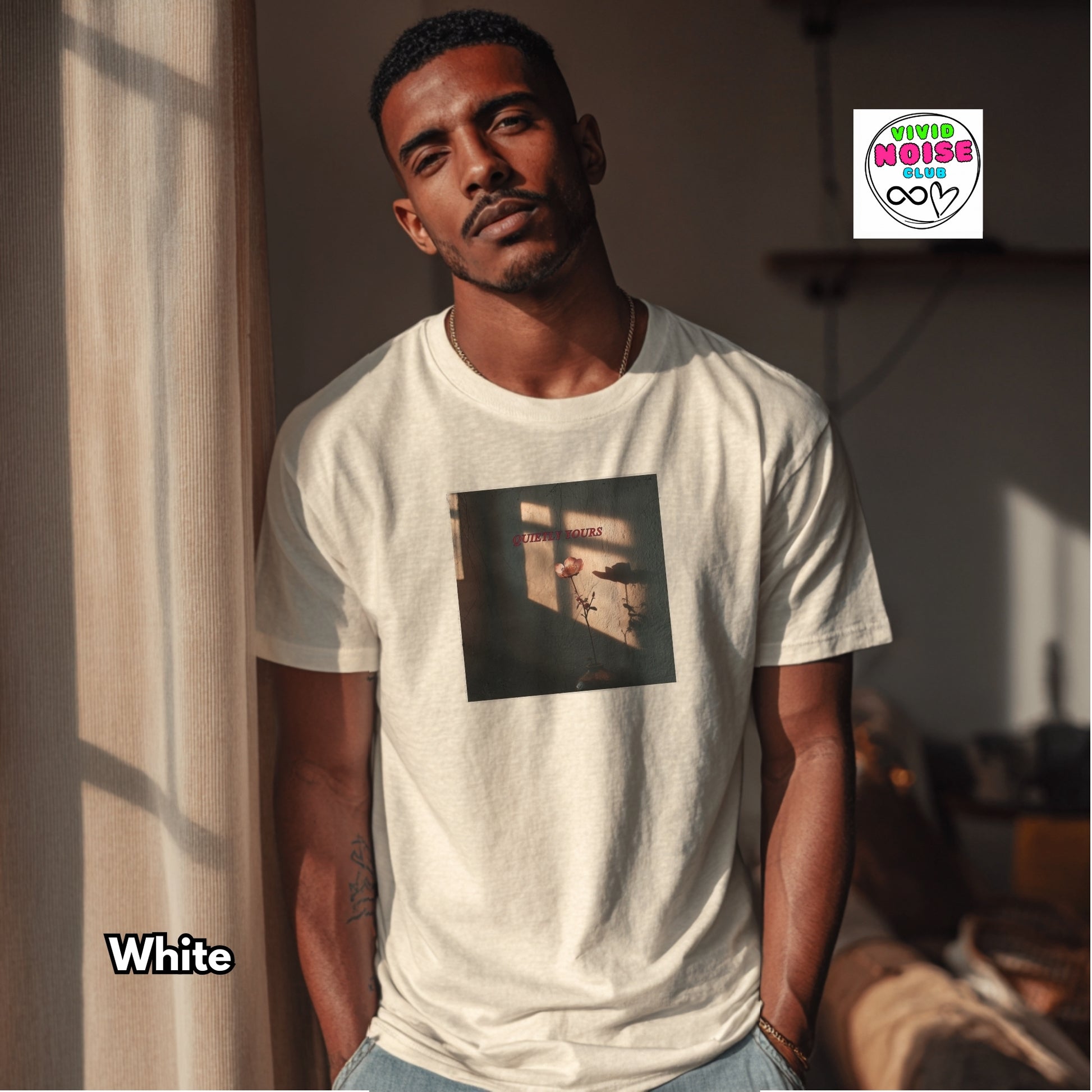 Man wearing a white t-shirt with a graphic design, standing in a room with sunlight filtering through curtains.