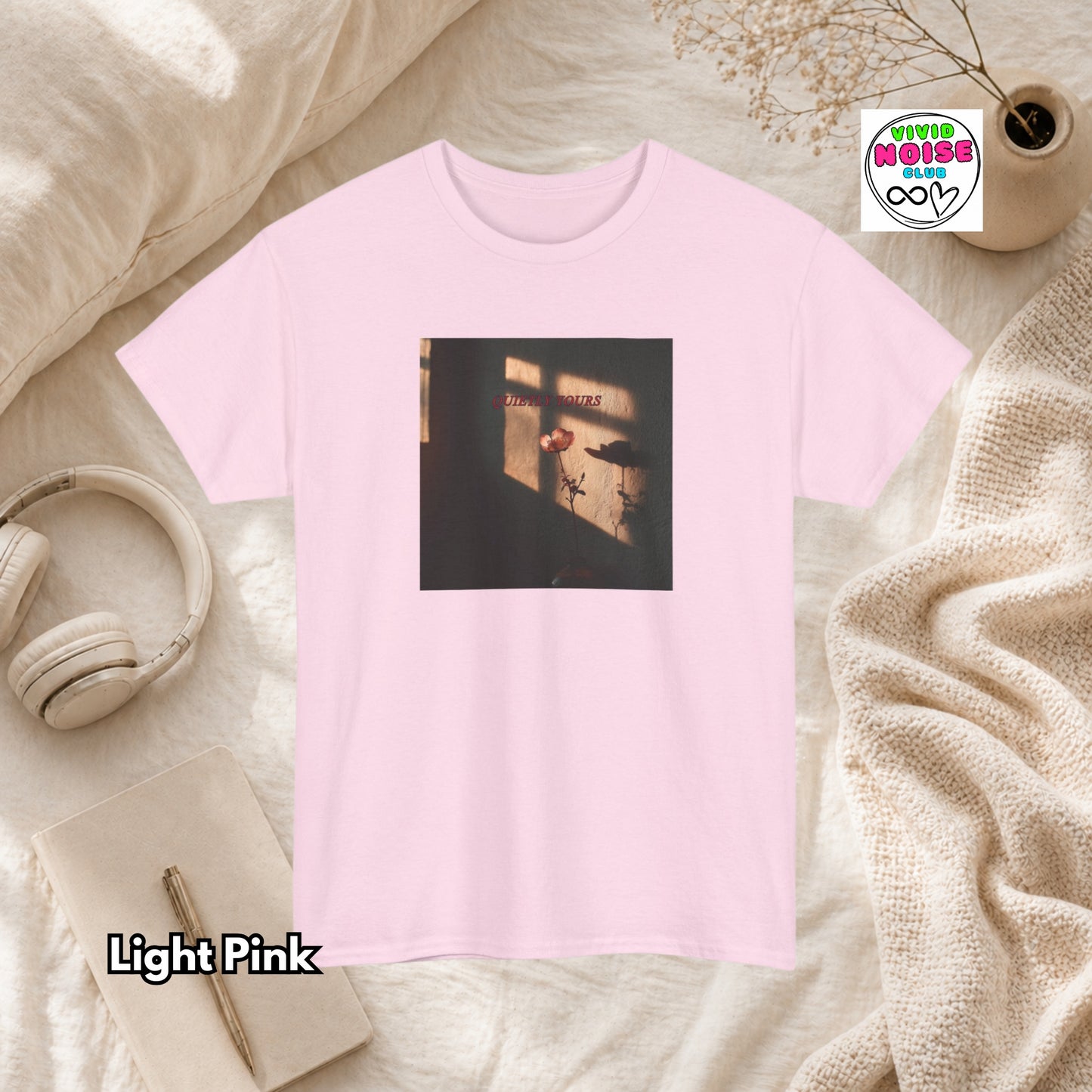 Light pink t-shirt with a graphic design on a soft surface with headphones and a notebook.