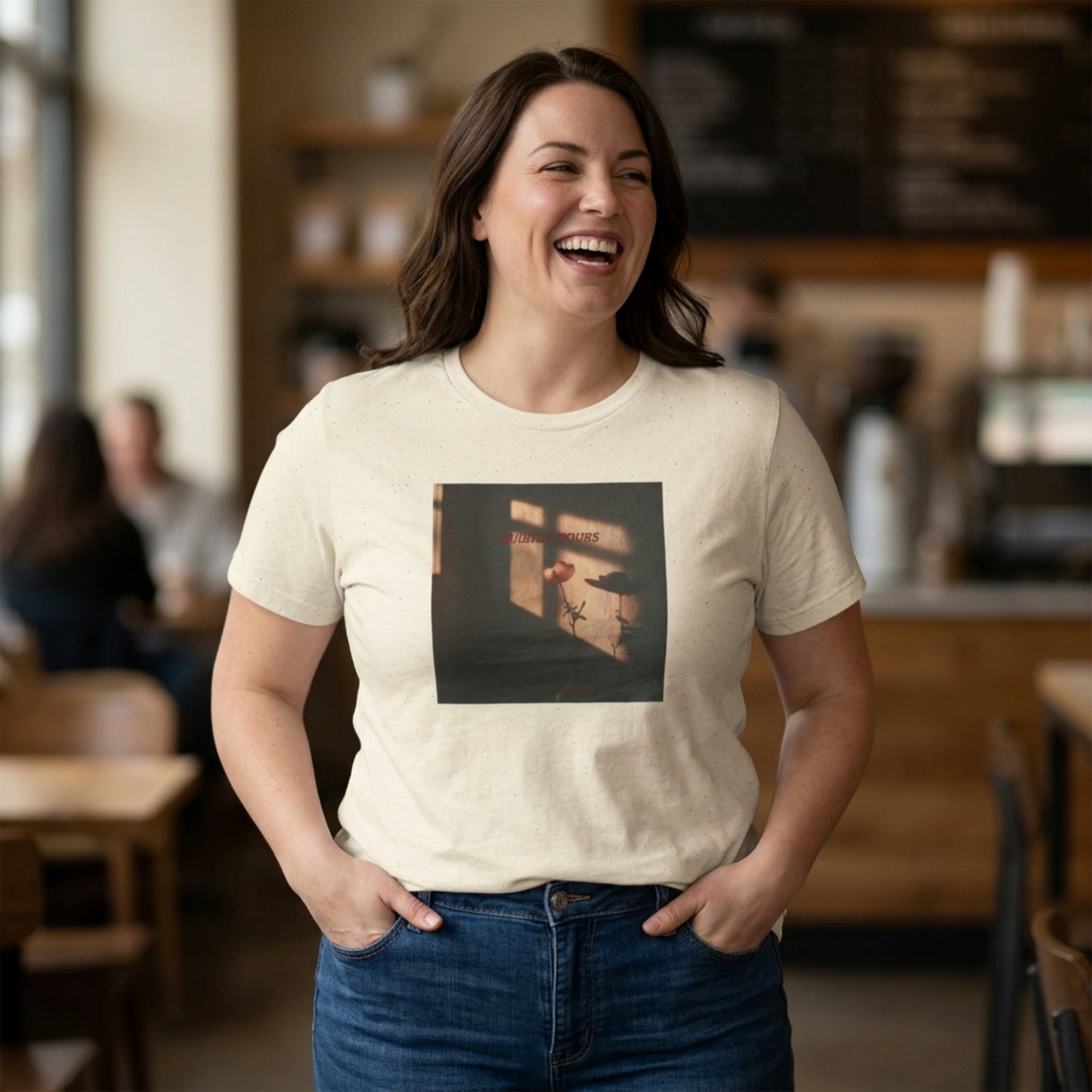 Woman wearing a cream t-shirt with a Quietly Yours floral graphic design, standing in a café casual setting.