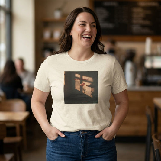Woman wearing a cream t-shirt with a Quietly Yours floral graphic design, standing in a café casual setting.