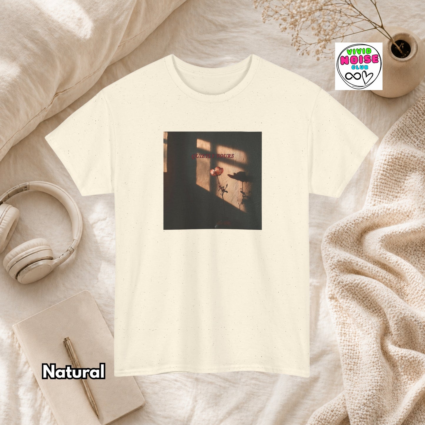 Natural beige t-shirt with Quietly Yours floral graphic design on a beige surface with headphones and a notebook.