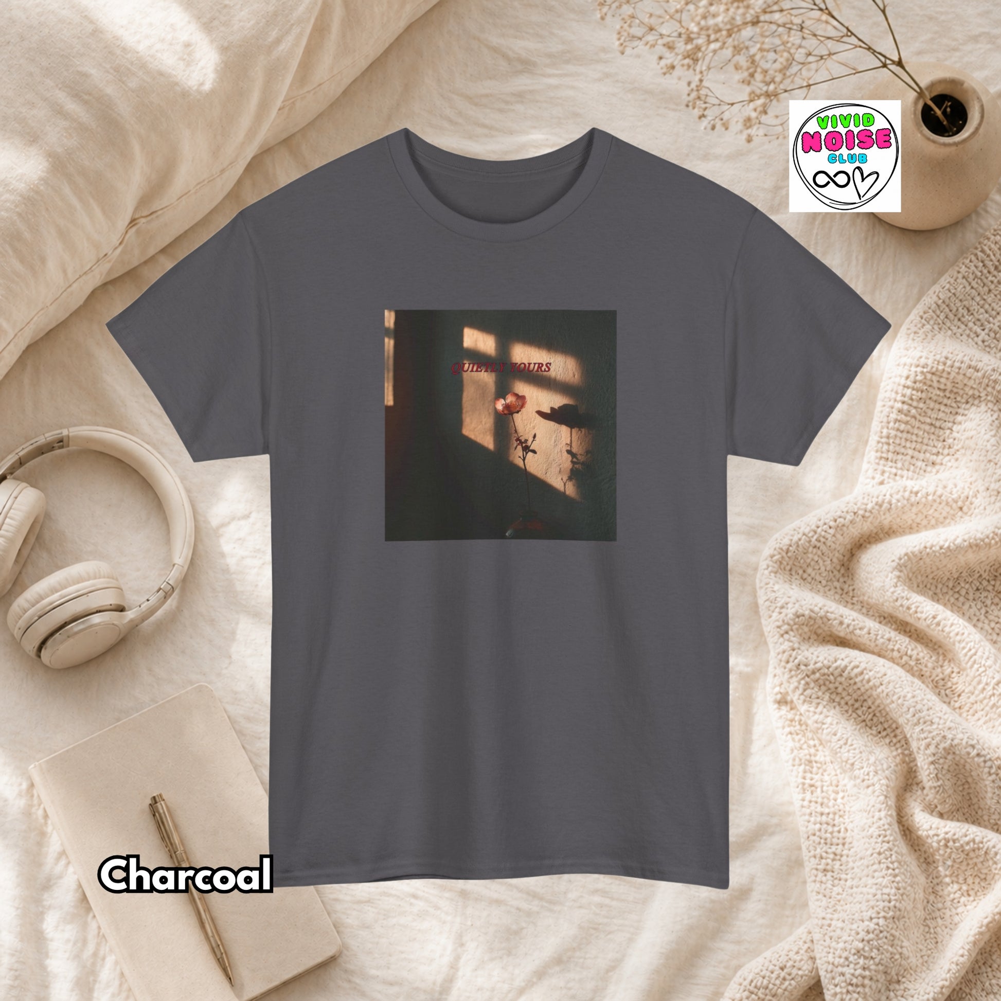 Charcoal gray t-shirt with a graphic design on a beige surface with headphones and a notebook.