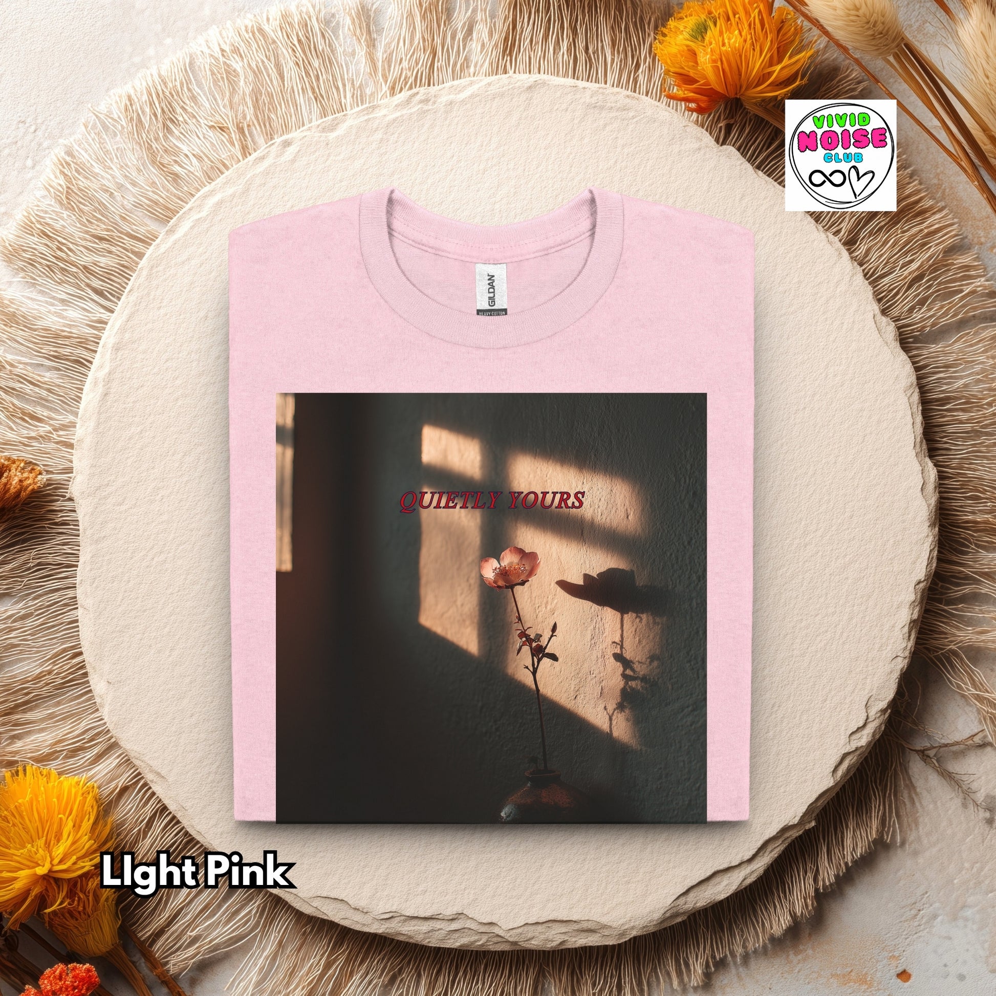 Light pink t-shirt with 'QUIETLY YOURS' design on a round beige pillow with flowers.