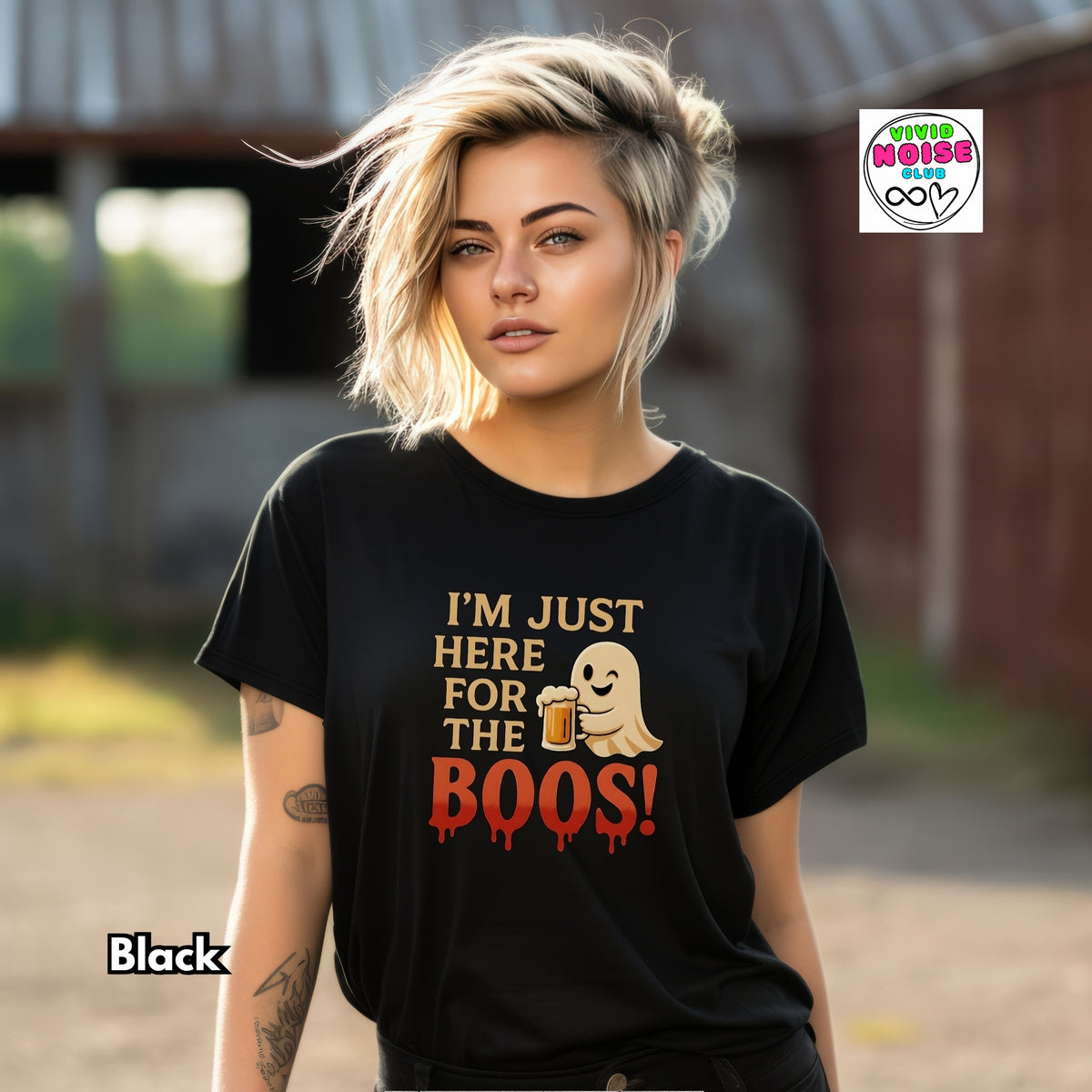 A woman wearing a black graphic t-shirt with the text 'I'M JUST HERE FOR THE BOOS!' and a ghost holding a beer mug. The background is a blurred outdoor barn setting.