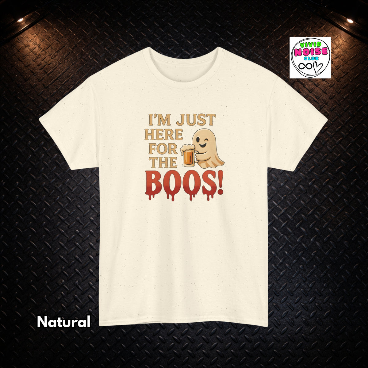A cream-colored short-sleeve t-shirt with a graphic print that reads 'I'M JUST HERE FOR THE BOOS!' in tan and dripping red letters, featuring a cute ghost holding a beer mug. The t-shirt is displayed flat against a dark textured diamond plate background with 'Natural' text overlay in the bottom-left corner and a 'Tired of Being Single' logo in the top-right corner.