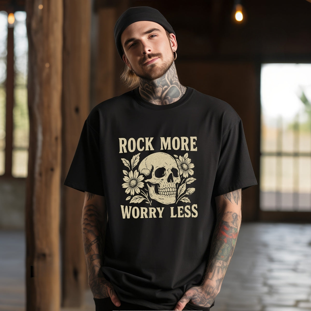A man wearing a black graphic t-shirt with a beige skull and floral design and the text 'ROCK MORE WORRY LESS', standing in a rustic indoor setting with wooden pillars.