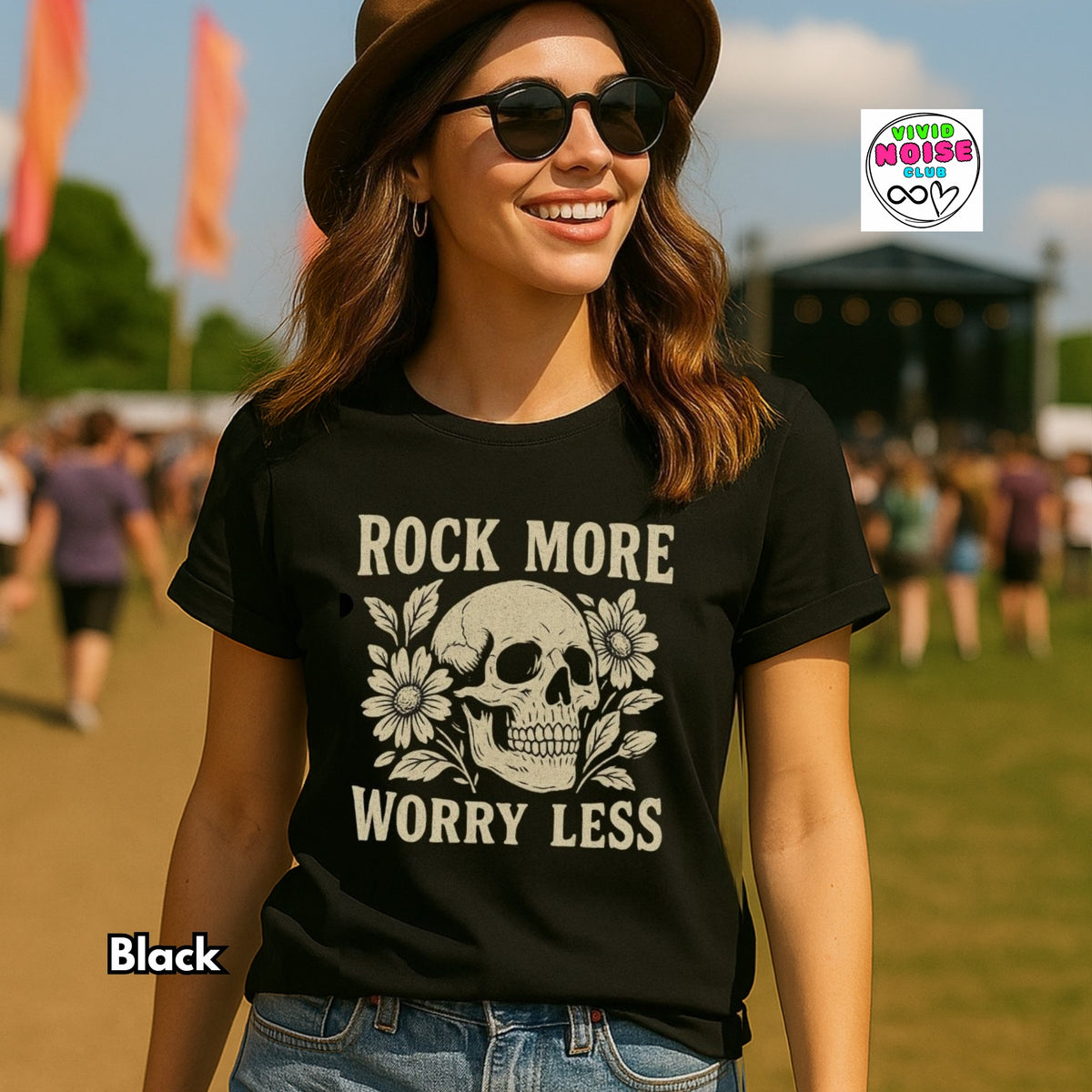 A woman outdoors wearing a black graphic T-shirt with a cream skull and floral design and the text 'ROCK MORE WORRY LESS.' She is also wearing a brown hat, sunglasses, and blue jeans.