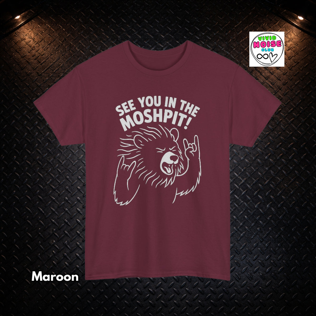 A maroon short-sleeve t-shirt with a white graphic of a bear making a hand gesture and the text 'SEE YOU IN THE MOSHPIT!' printed on the chest. The t-shirt is displayed against a dark textured diamond plate background with dramatic overhead lighting, a 'Vivid Noise Club' logo in the top right, and the word 'Maroon' in the bottom left.