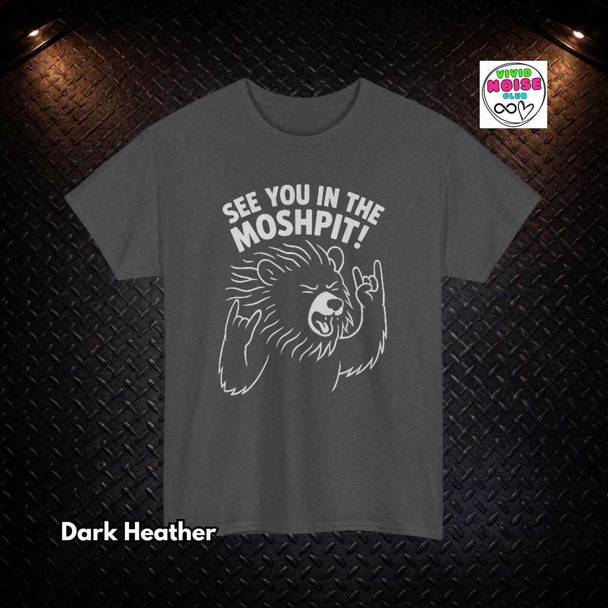 A dark heather gray t-shirt with a white graphic of a bear making a hand gesture and the text 'SEE YOU IN THE MOSHPIT!'. The t-shirt is displayed flat against a black diamond plate background with dramatic overhead lighting, featuring a 'Vivid Noise Club' logo in the top right and 'Dark Heather' text in the bottom left.