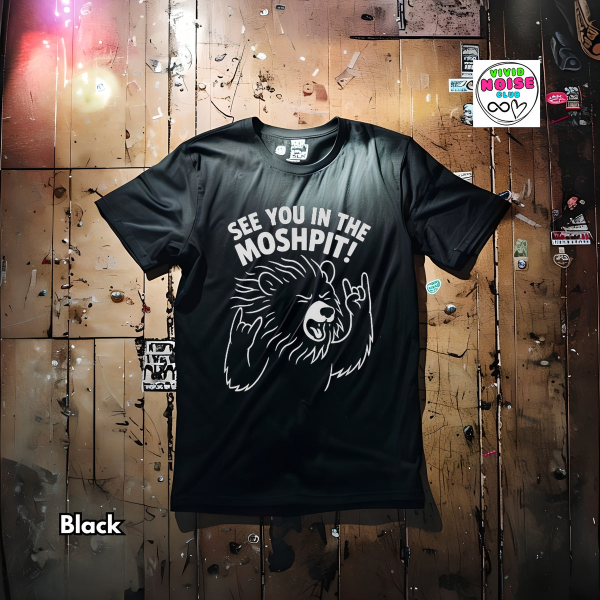 A black short-sleeve graphic T-shirt laid flat on a distressed wooden plank background. The shirt has a white line-art bear graphic and the text 'SEE YOU IN THE MOSHPIT!' across the chest.