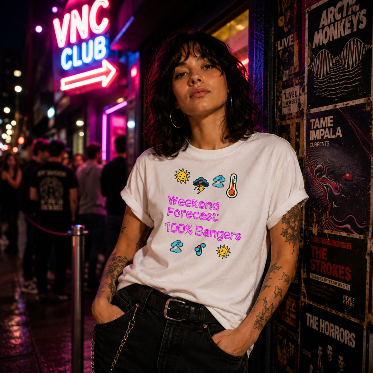 A woman wearing a white graphic t-shirt with colorful weather icons and the text 'Weekend Forecast: 100% Bangers' stands in a neon-lit city setting next to a wall of band posters.