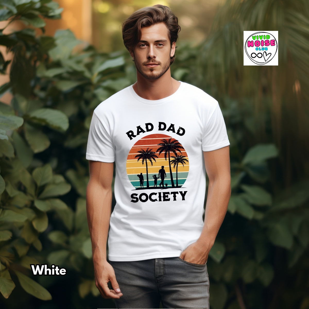 A man wearing a white graphic t-shirt with a retro sunset design and the text 'RAD DAD SOCIETY'. The background is a lush, blurred green garden.