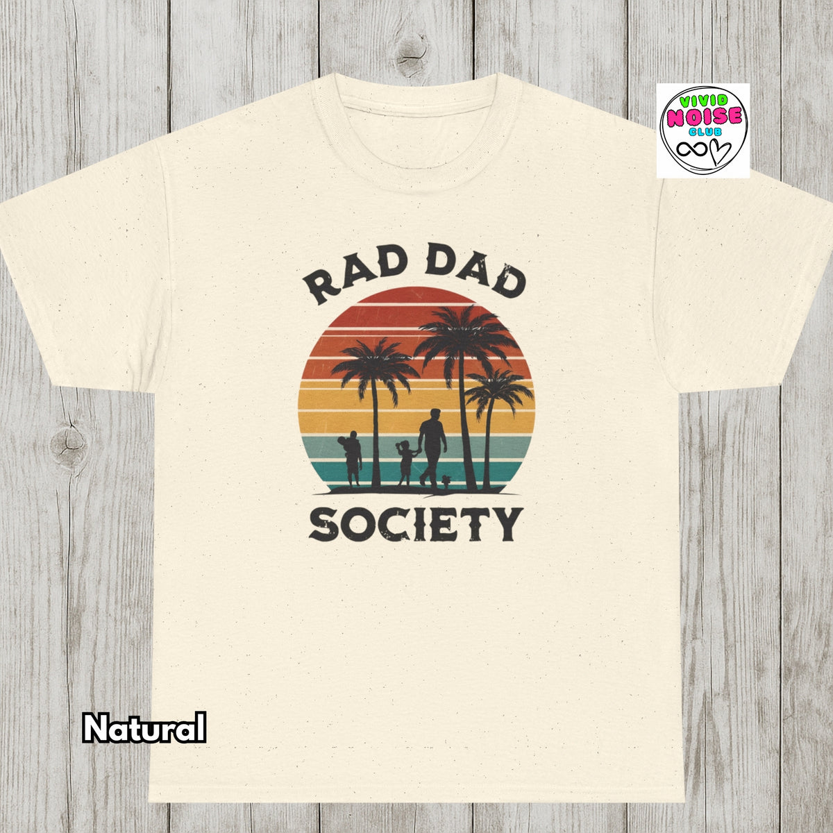 A cream-colored t-shirt with a retro sunset graphic featuring palm trees and a family silhouette, with the text 'RAD DAD SOCIETY' printed on the front. The t-shirt is displayed flat against a gray wood-plank background, with a 'Natural' color label in the bottom-left corner and a 'Vivid Noise Club' brand logo in the top-right corner.