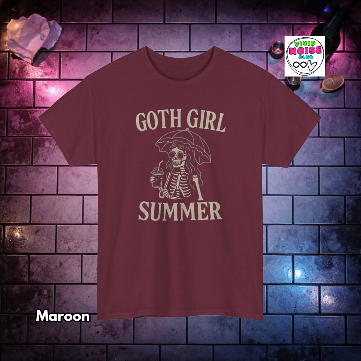 A maroon short-sleeve t-shirt with a cream-colored graphic of a skeleton under an umbrella holding a drink, with the text 'GOTH GIRL SUMMER'. The shirt is displayed against a dark brick wall background with purple and blue lighting, with a 'Vivid Noise Club' logo in the top right and 'Maroon' text in the bottom left.