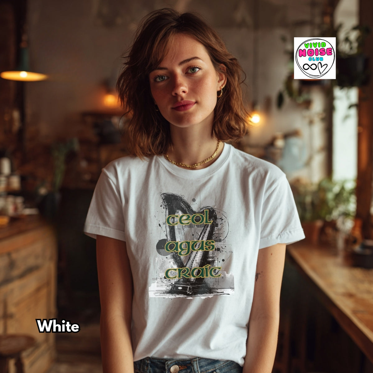 A woman wearing a white graphic t-shirt with a black and gray print and green text reading 'Ceol Agus Craic', set in a warm, rustic indoor environment. A 'Vivid Noise Club' logo is visible in the top right, and the word 'White' is written in the bottom left.