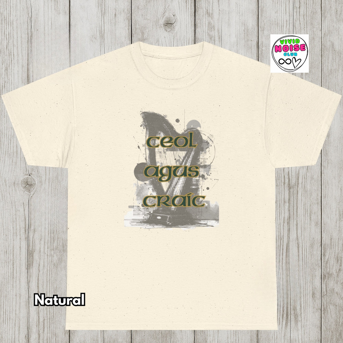 A natural cream-colored t-shirt with a distressed graphic of a violin and the text 'Ceol Agus Craic' in olive green, displayed on a gray wood plank background with a 'Vivid Noise Club' logo in the top right and 'Natural' text in the bottom left.