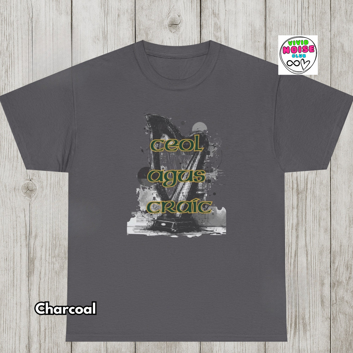 A charcoal gray t-shirt with a black and white graphic of a guitar and the words 'Ceol Agus Craic' in yellow-green text, displayed flat on a light wood background with a 'Charcoal' label and a 'Vivid Noise Club' logo.