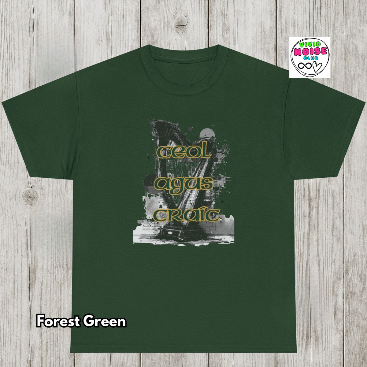 A forest green short-sleeve t-shirt laid flat on a light gray wood plank background. The center of the shirt features a black-and-white graphic of a harp with the words 'Ceol Agus Craic' in yellow outlined letters.
