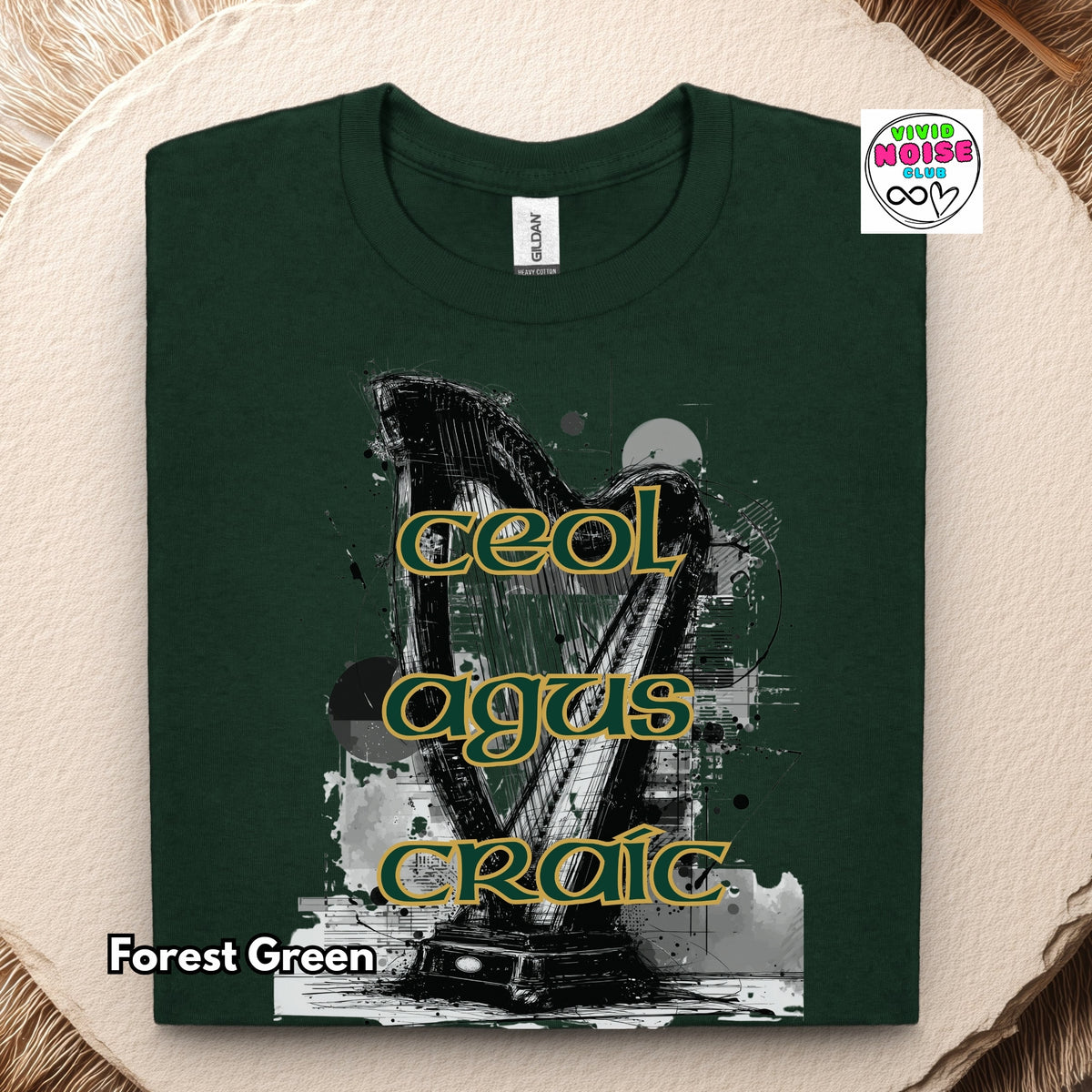 A folded forest green t-shirt with a graphic of a harp and the Irish phrase 'Ceol agus Craic' in yellow outlined lettering, displayed on a textured beige background with a 'Vivid Noise Club' brand sticker.
