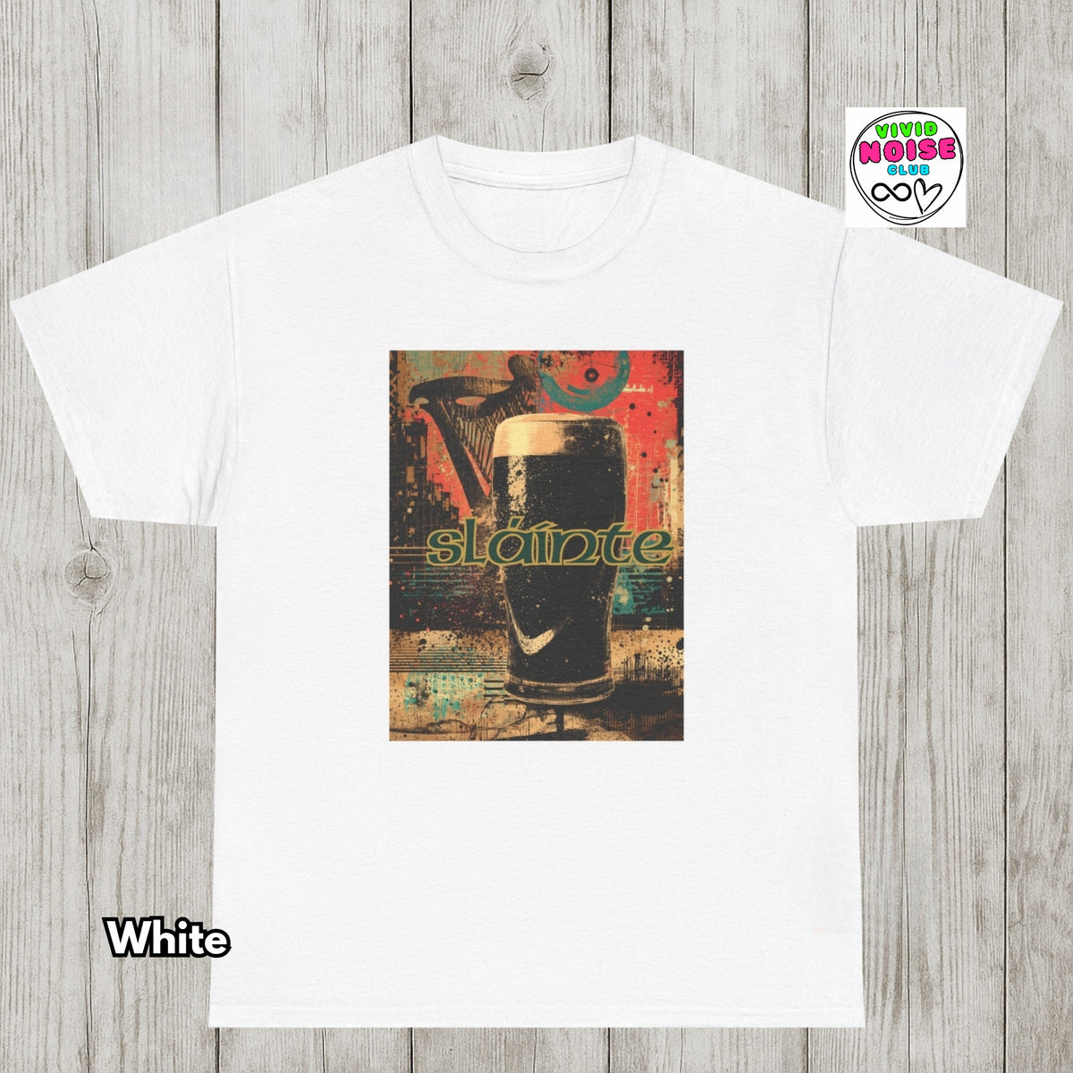 A white short-sleeve crewneck t-shirt laid flat on a light gray wood plank background. The center of the shirt features a rectangular graphic print of a dark beer glass with the word 'Slainte' in green.