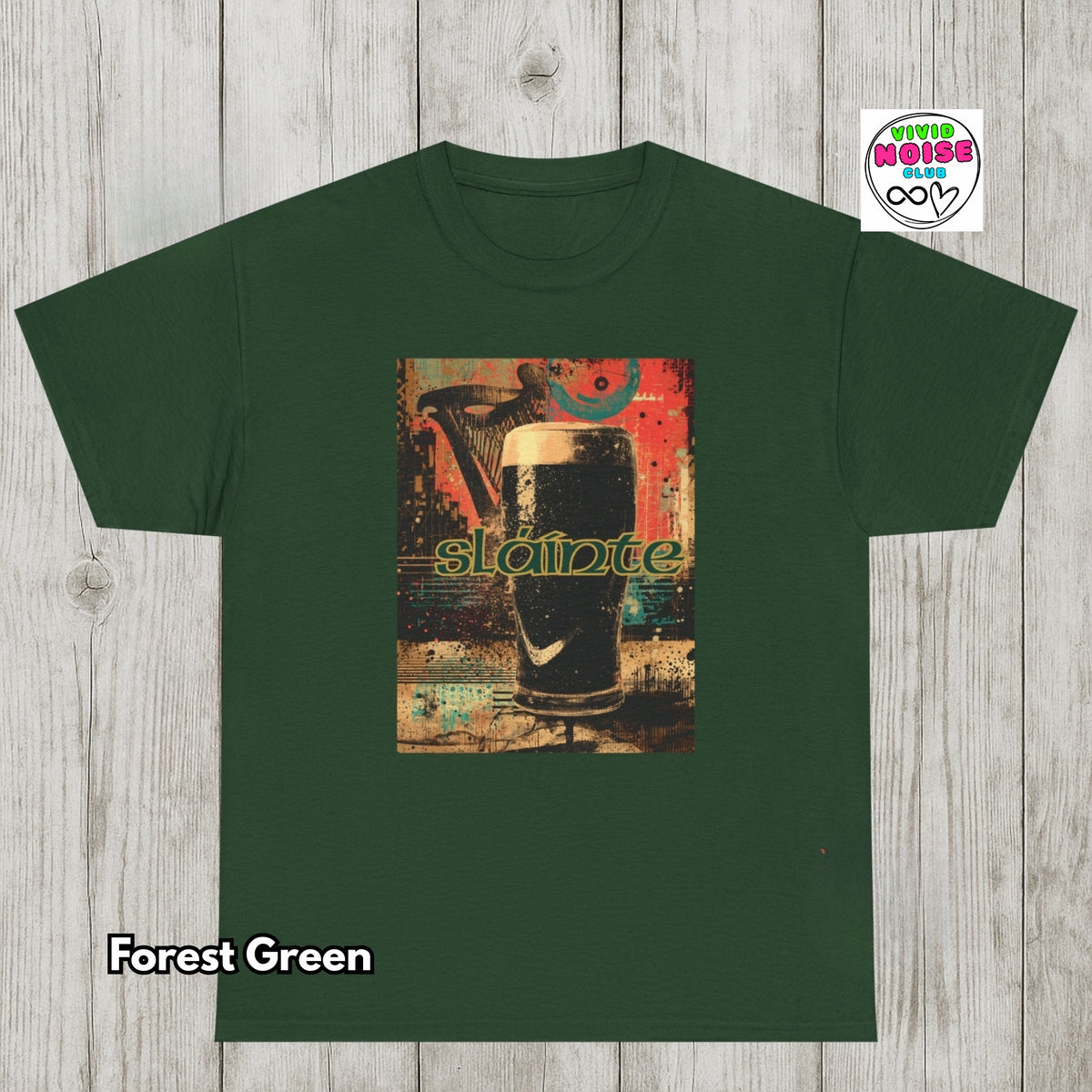 A forest green short-sleeve t-shirt laid flat on a light gray wood plank background. The center of the shirt features a rectangular graphic print of a pint of dark stout beer with the word 'slainte' in green text.