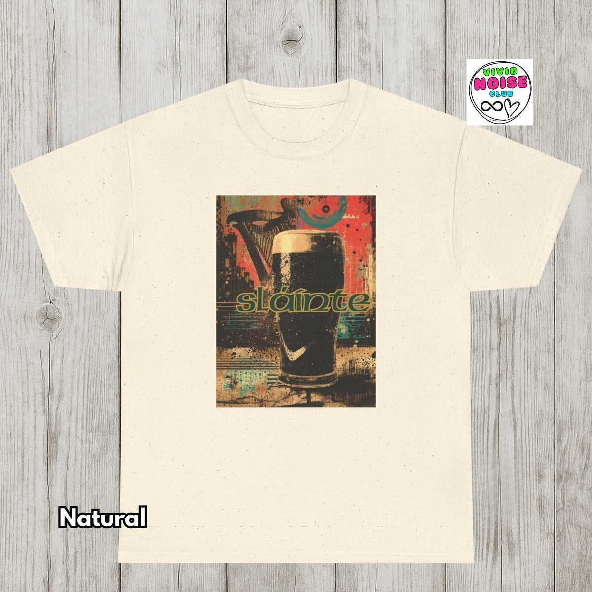 A cream-colored t-shirt with a central graphic print of a pint of stout with the word 'Slainte' in green, displayed on a gray wood plank background. A 'Natural' label is visible in the bottom-left corner, and a 'Vivid Noise Club' logo top-right.