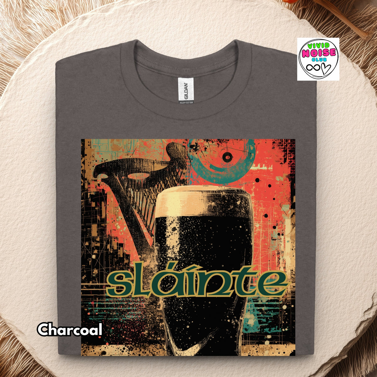 A charcoal gray folded t-shirt with a colorful graphic print of a pint of stout and the word 'sláinte' in green, displayed on a round wooden coaster with a fur texture background.