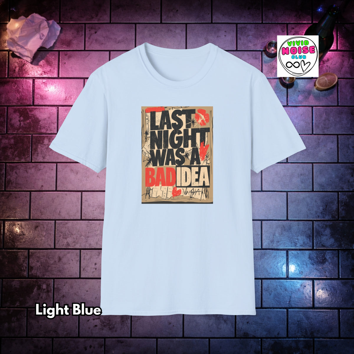 A light blue short-sleeve t-shirt with a graphic print on the front that reads 'LAST NIGHT WAS A BAD IDEA' in black, red, and beige. The shirt is displayed against a dark brick wall background with purple and blue lighting, with a 'Vivid Noise Club' logo in the top right corner and 'Light Blue' text in the bottom left.