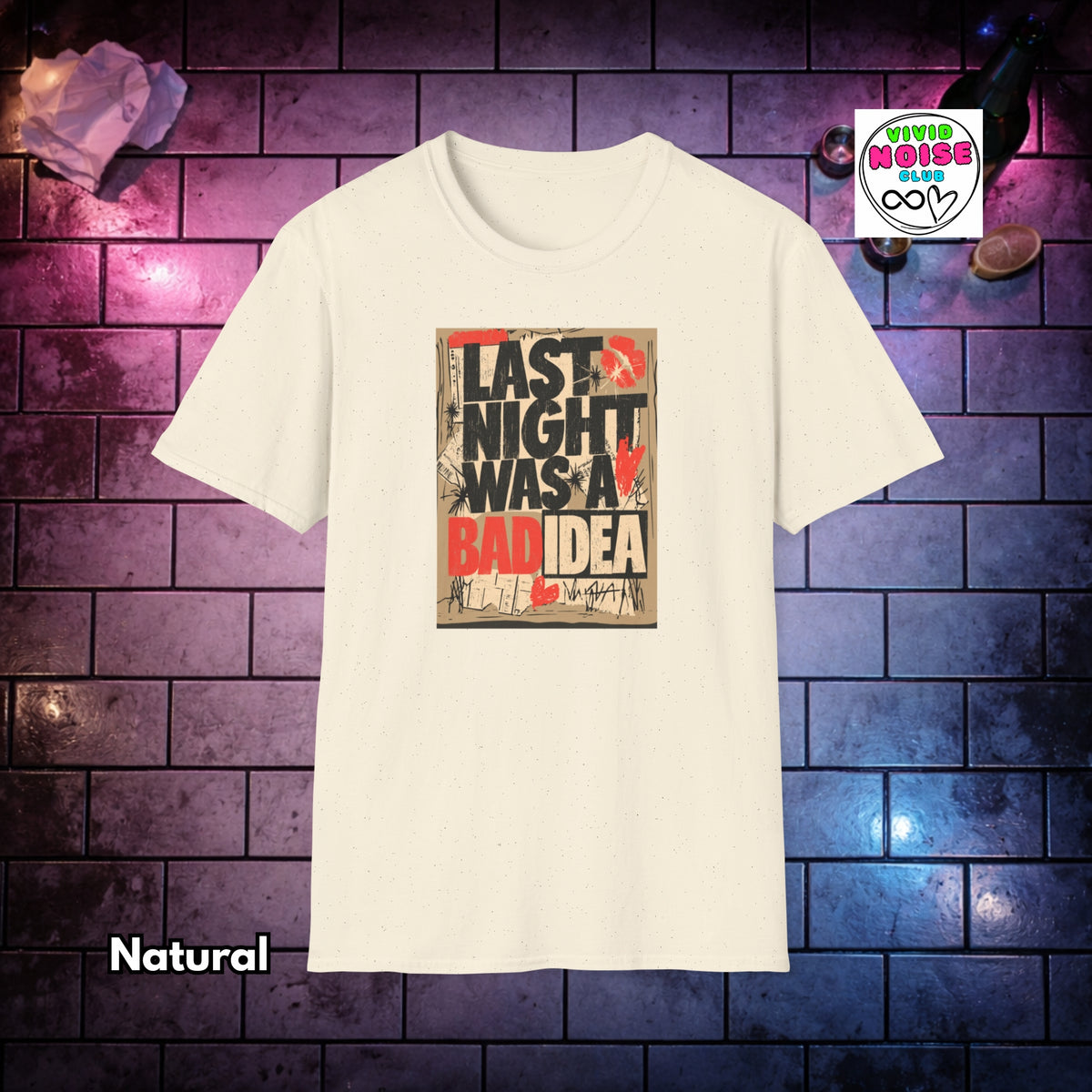 A cream-colored short-sleeve t-shirt with a graphic print on the front that reads 'LAST NIGHT WAS A BAD IDEA' in black and red text over a distressed beige background. The t-shirt is displayed against a dark brick wall background with purple and blue lighting, with a 'Vivid Noise Club' logo in the top right corner and the word 'Natural' in the bottom left.