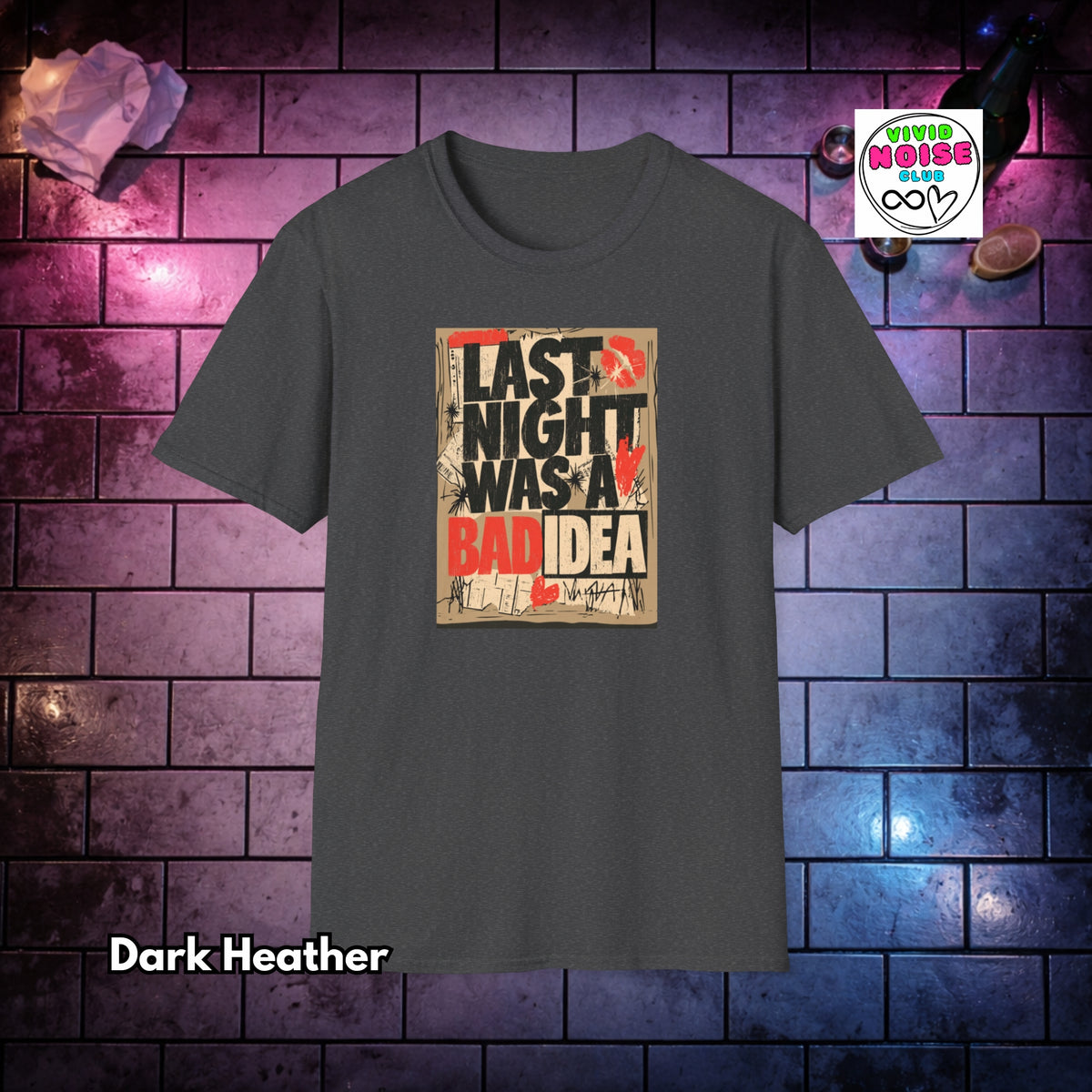 A dark heather gray t-shirt with a graphic print reading 'LAST NIGHT WAS A BAD IDEA' in black and red text on a beige background. The shirt is displayed against a purple and blue brick wall background with decorative props, and a 'Vivid Noise Club' logo is visible in the top right.