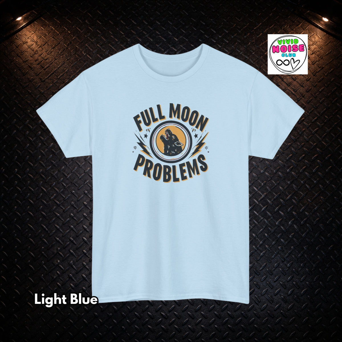 A light blue short-sleeve t-shirt with a graphic on the chest that reads 'FULL MOON PROBLEMS' in a circular design. The t-shirt is displayed flat against a dark textured diamond plate background with warm overhead lights, a 'Vivid Noise Club' logo in the top right, and 'Light Blue' text in the bottom left.
