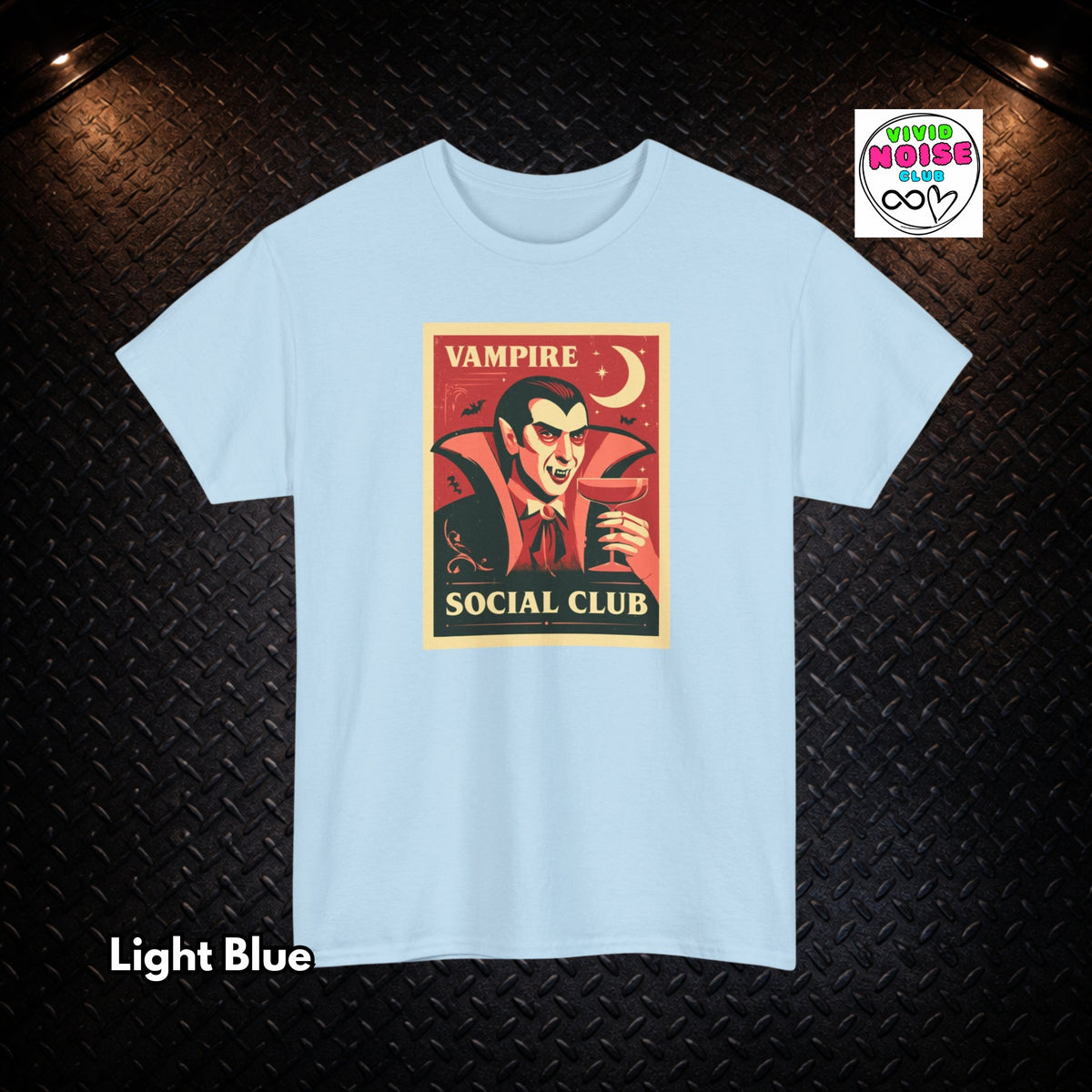 A light blue short-sleeve t-shirt with a vintage-style vampire graphic on the chest, displayed on a dark textured background with 'Light Blue' text overlay in the bottom left and a 'Vivid Noise Club' logo in the top right.