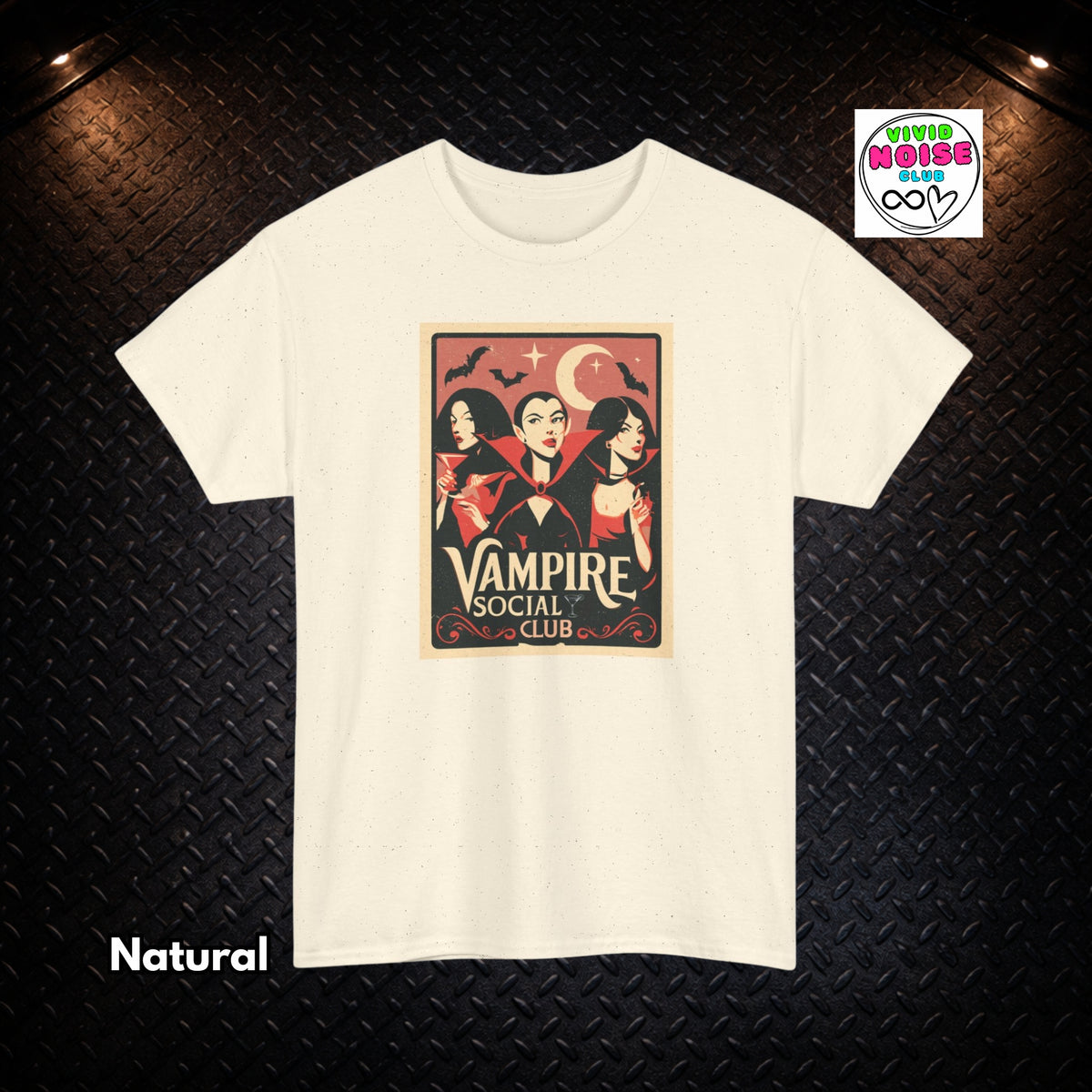 An off-white/cream t-shirt with a vintage-style graphic print of three vampires under a crescent moon and stars, labeled 'Vivid Noise Club'. The t-shirt is displayed flat against a dark textured diamond plate background with dramatic overhead lights.