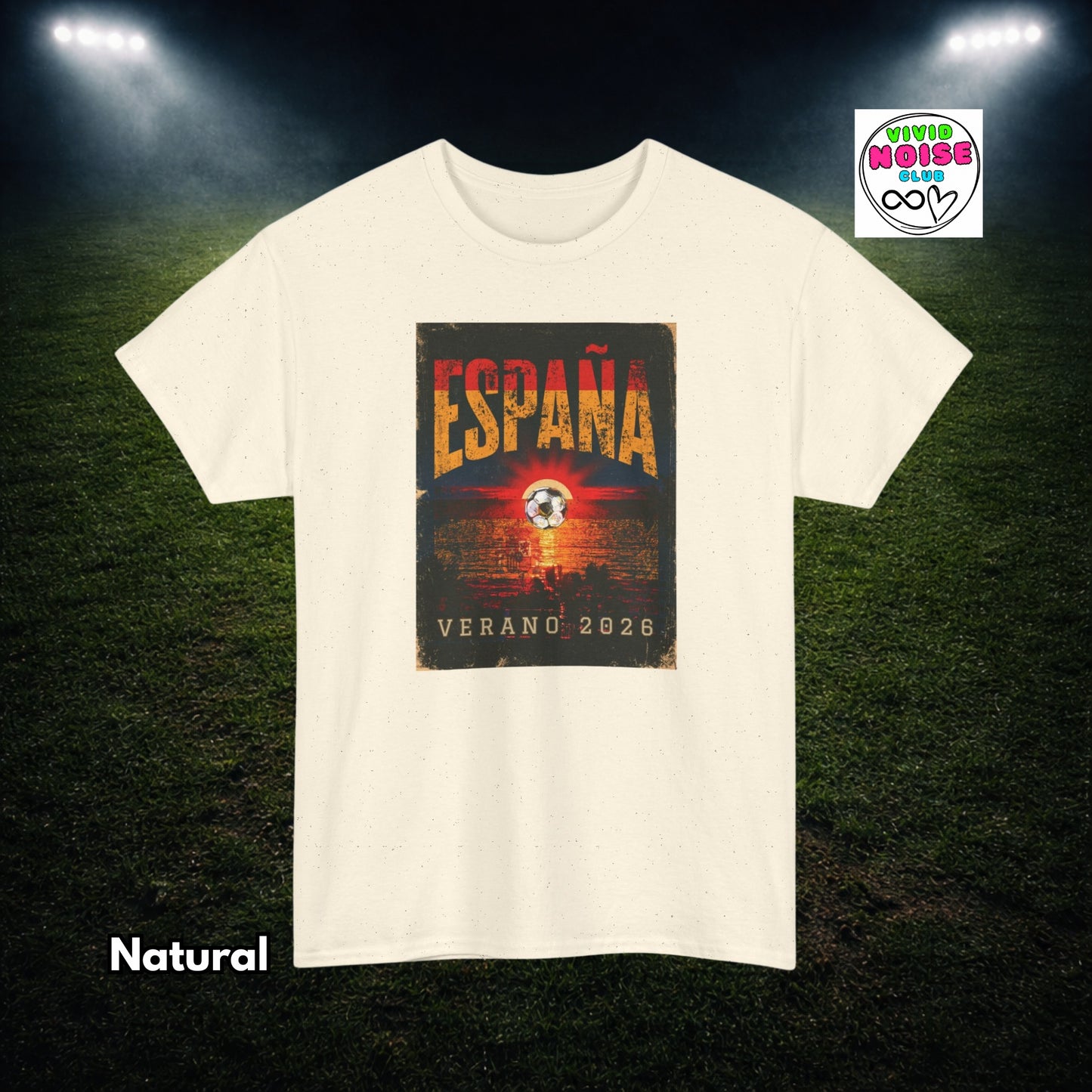 A cream-colored short-sleeve t-shirt with a distressed graphic on the front that reads 'ESPAÑA VERANO 2026' in orange and red lettering over a dark background. The t-shirt is displayed against a dark green soccer field background with stadium lights shining down, with 'Natural' text in the bottom-left corner.